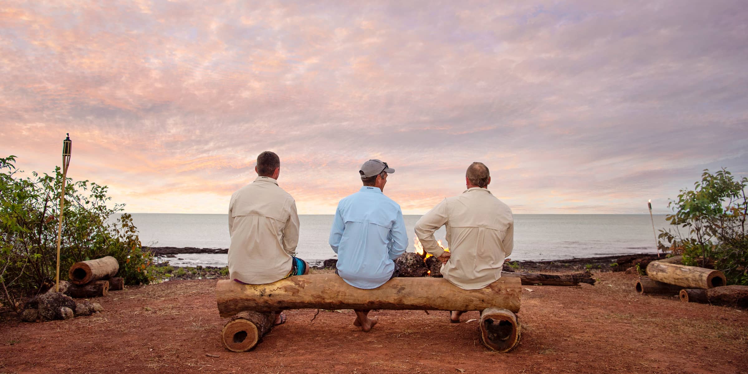 Three men sitting on log looking at water